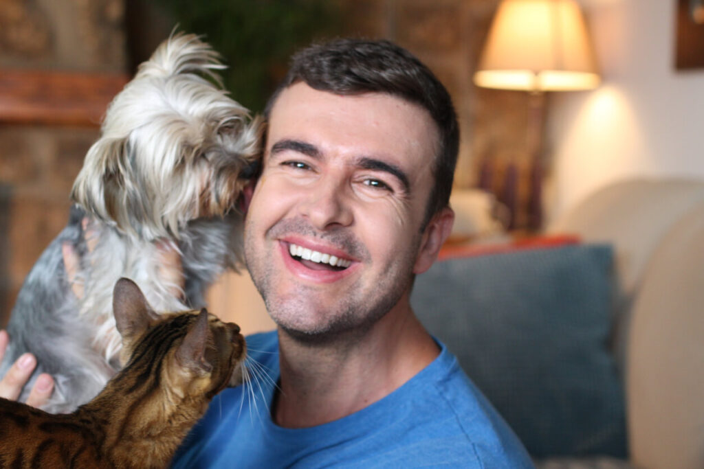 Handsome man smiles as he cuddles his cat and small fluffy dog